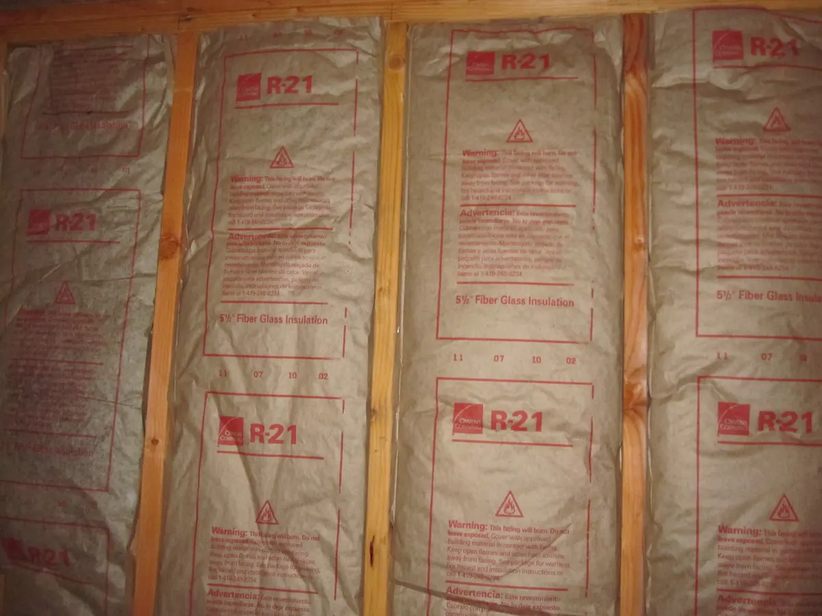 Kraft-faced fiberglass batts installed between wall studs, with R-21 printed repeatedly on the brown facing
